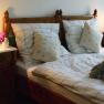 Gemütliches Doppelzimmer mit Holzmöbeln, Bett mit kariertem Bettzeug, Nachttischen und Lampen.