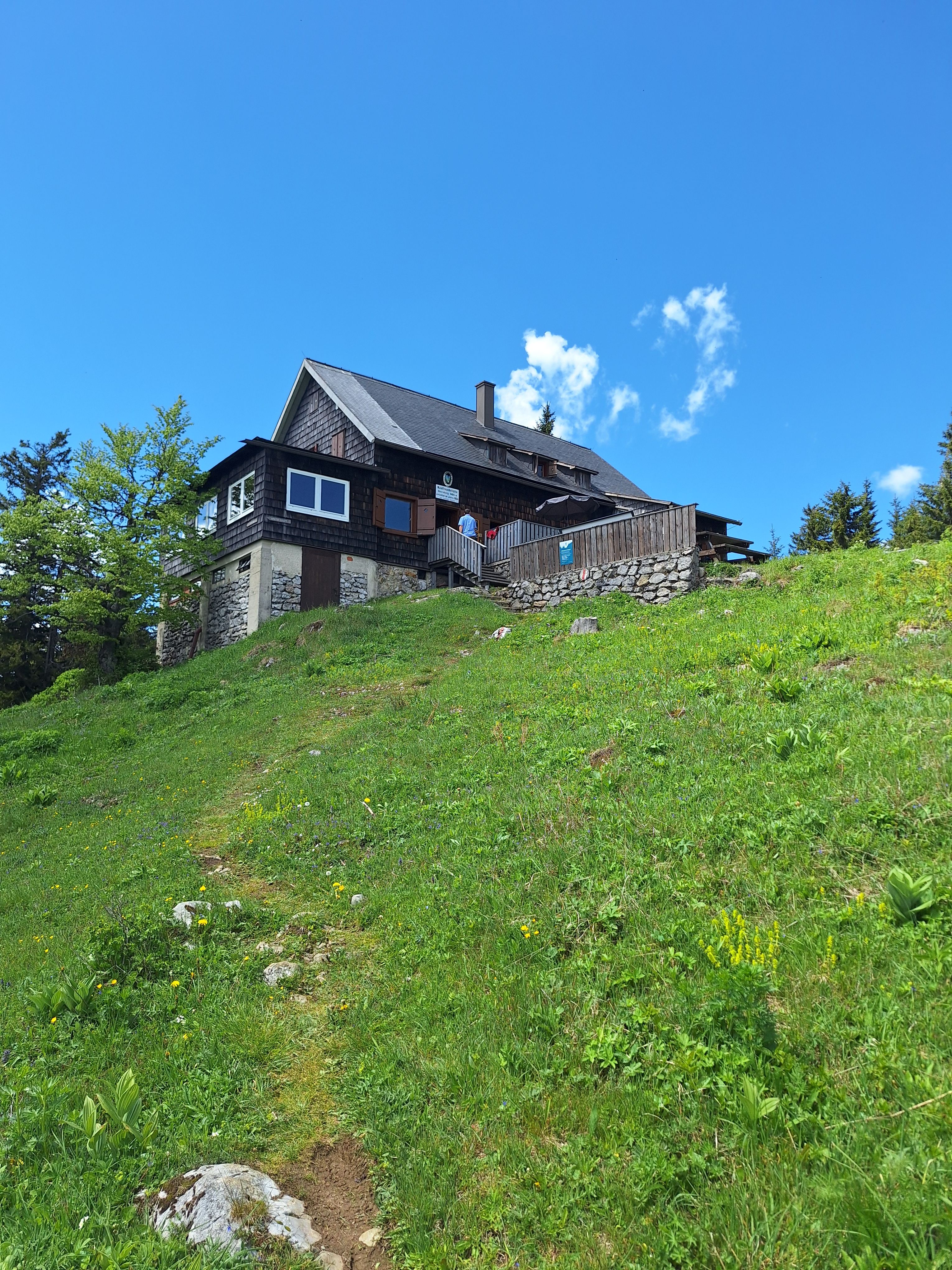 Eine Berghütte auf einer grünen Wiese unter blauem Himmel.