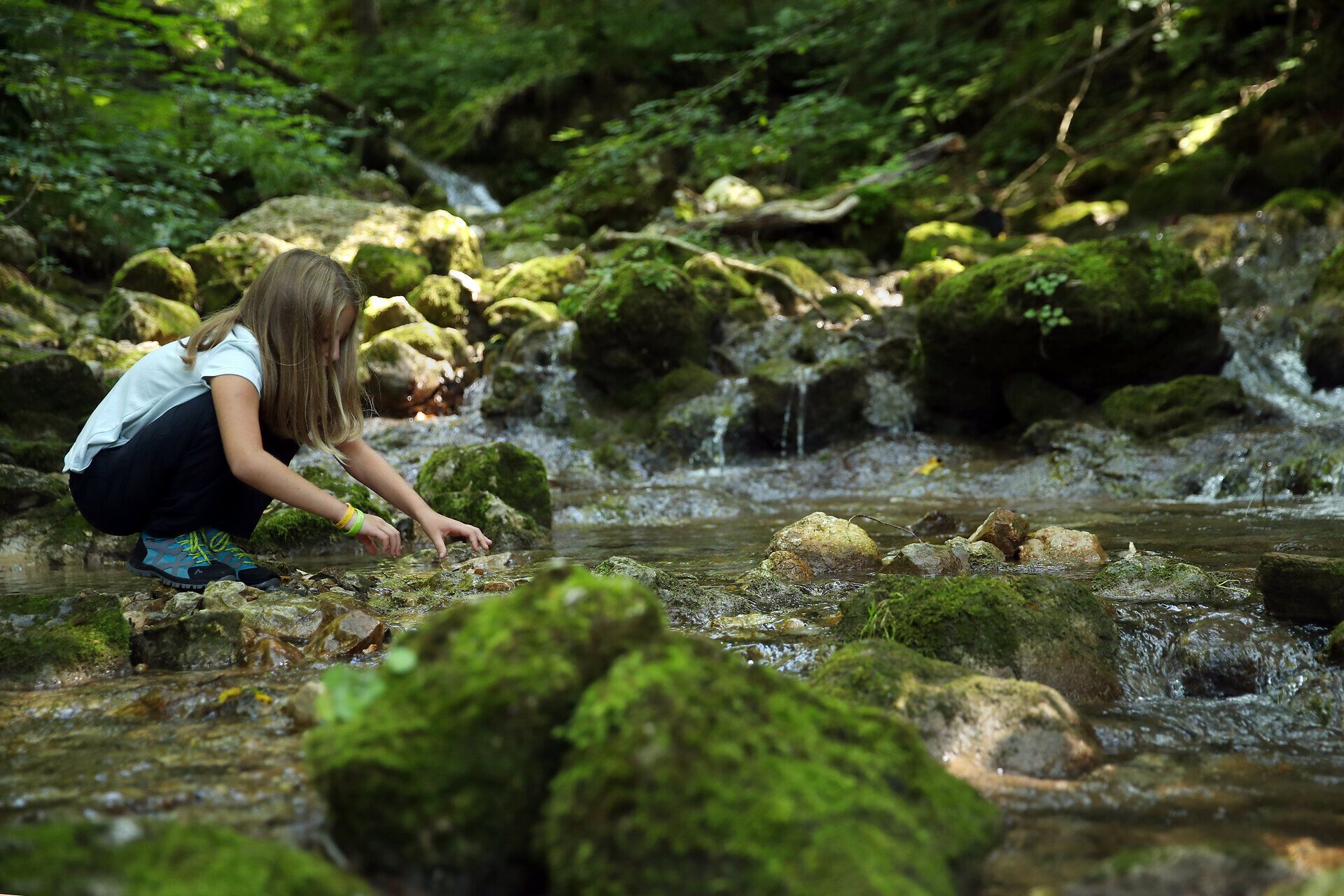 Ein Mädchen spielt an einem Bach im Naturpark Falkenstein. 