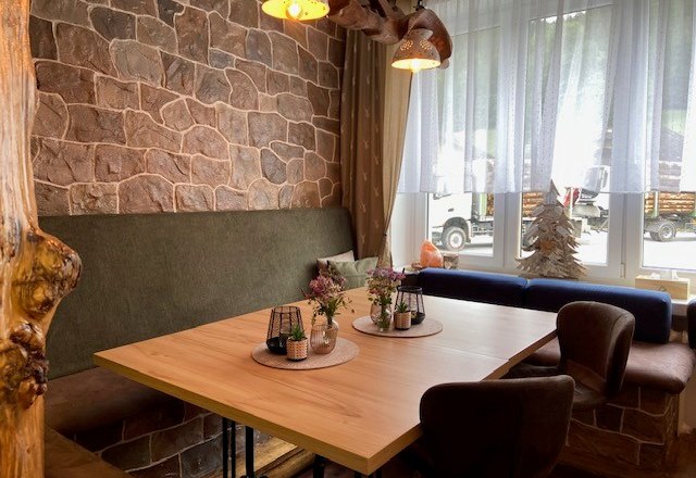 Gem&uuml;tliche Sitzecke in einem Hofladen mit Holztisch, gepolsterten St&uuml;hlen und Dekorationen auf dem Tisch.