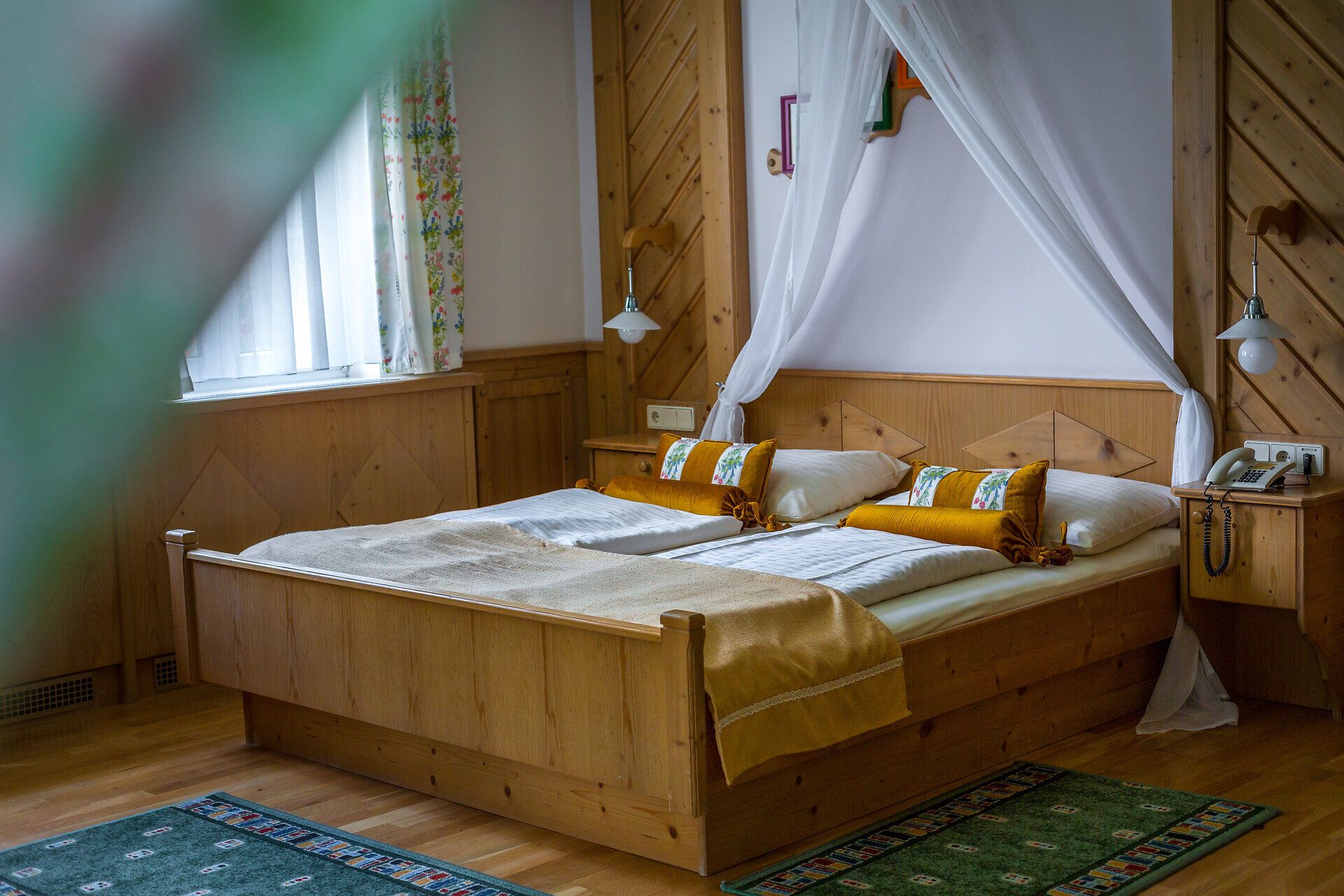 In den Zimmern im Hotel Raxalpenhof steht ein Holzbett mit Baldachin.