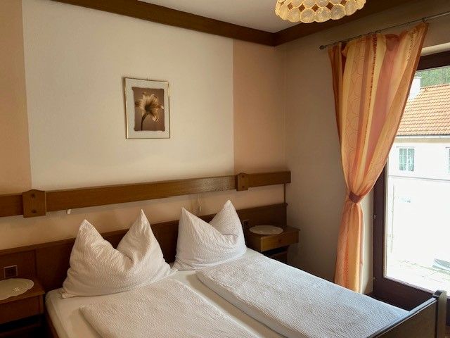 Ein gemütliches Doppelzimmer mit zwei Betten, einem Fenster mit Vorhang und einem Bild an der Wand.