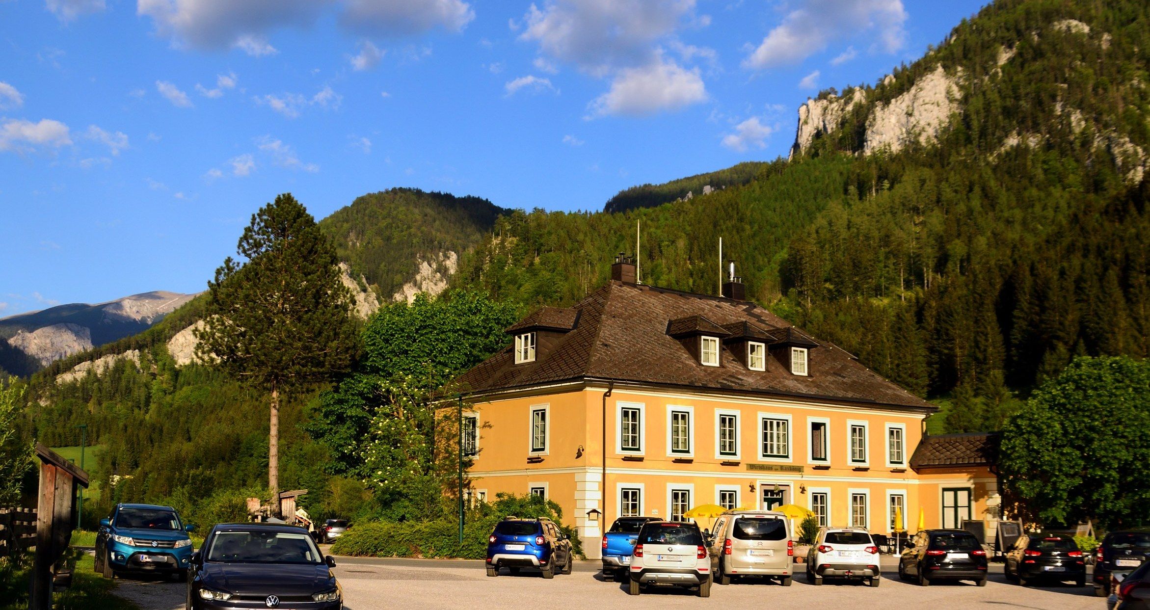 Ein gelbes Gebäude vor einer Bergkulisse mit geparkten Autos davor.