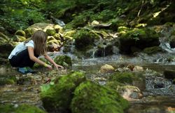 Ein Mädchen spielt an einem Bach im Naturpark Falkenstein. 