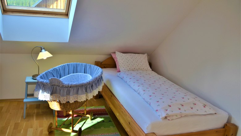 Ein gem&uuml;tliches Schlafzimmer mit Einzelbett, Babywiege und Dachfenster.