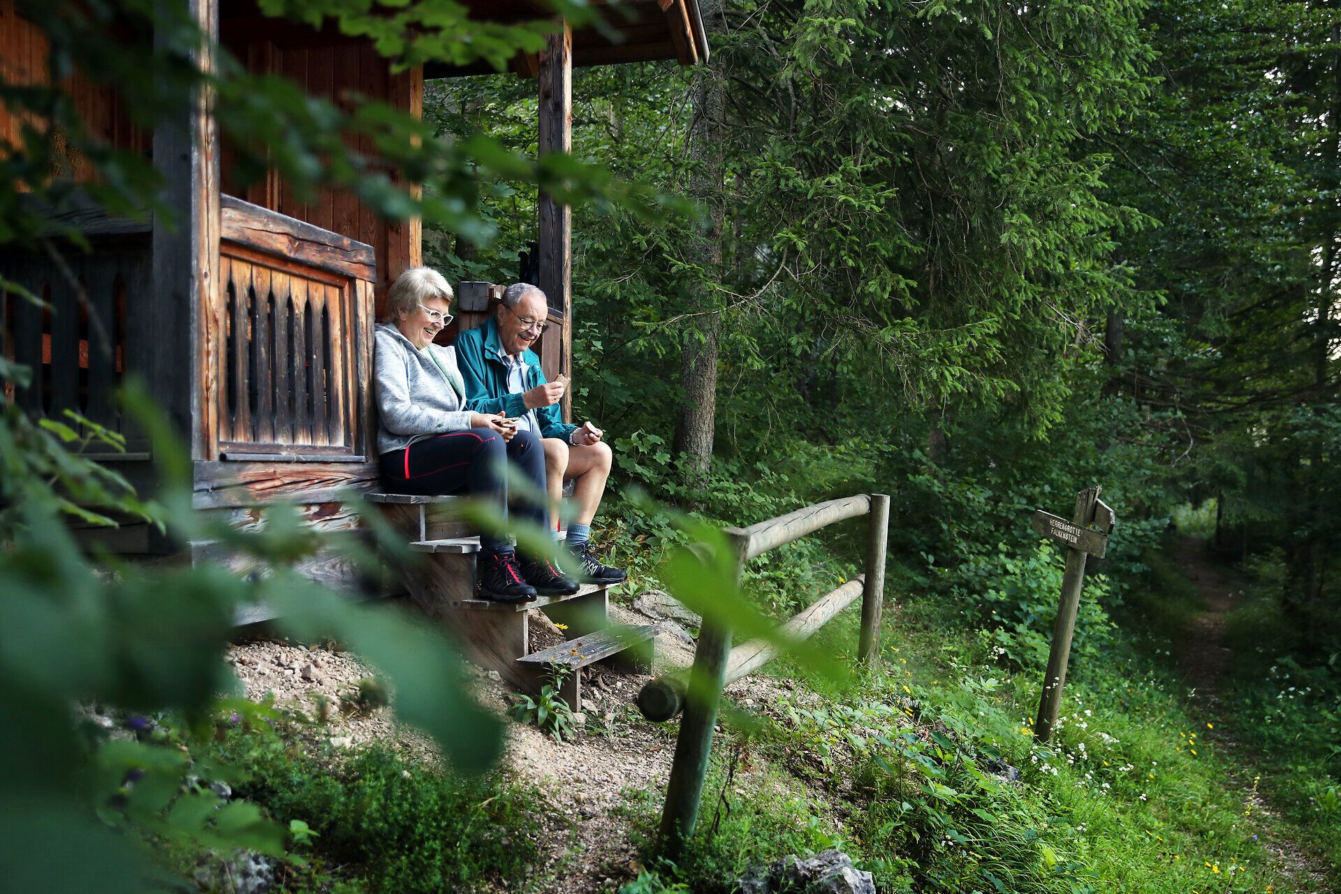 Ein Paar sitzt auf den Stufen einer kleinen Hütte und isst eine Jause im Naturpark Falkenstein. 