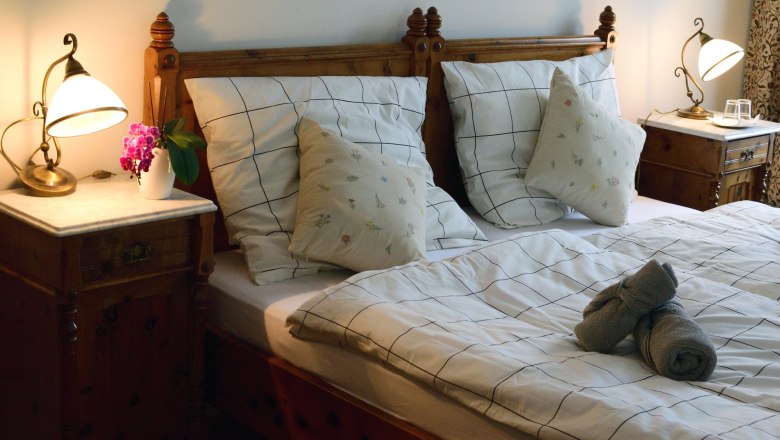 Gemütliches Doppelzimmer mit Holzmöbeln, Bett mit kariertem Bettzeug, Nachttischen und Lampen.