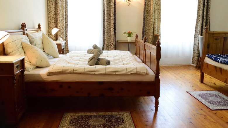 Gem&uuml;tliches Schlafzimmer mit Holzbett, Nachttischen und dekorativen Handt&uuml;chern auf dem Bett.