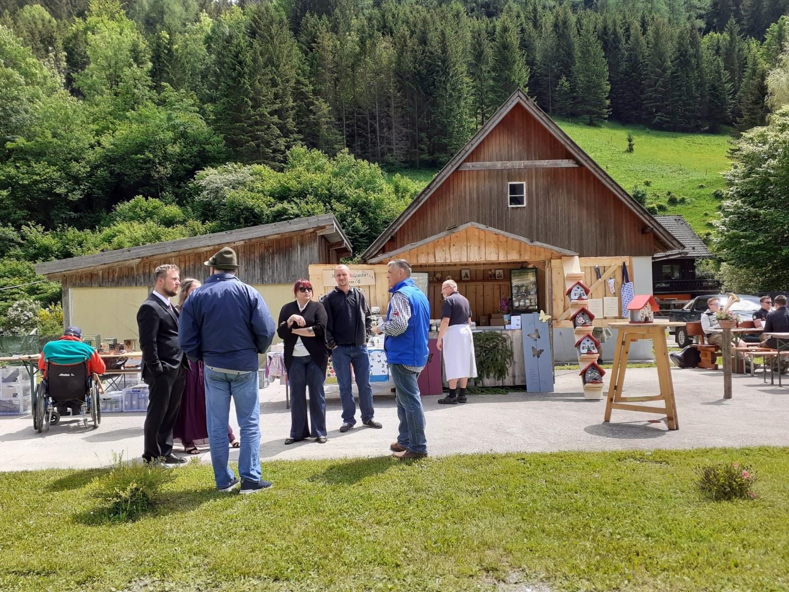 Menschen auf einem Markt vor Holzhütten in ländlicher Umgebung.