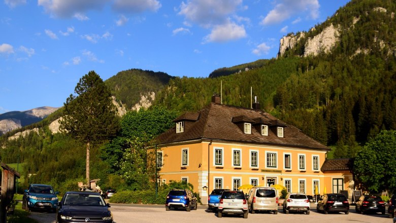 Ein gelbes Gebäude vor einer Bergkulisse mit geparkten Autos davor.