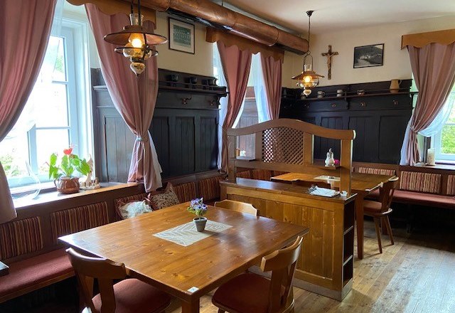 Gem&uuml;tliche Gaststube mit Holzm&ouml;beln und rosa Vorh&auml;ngen.
