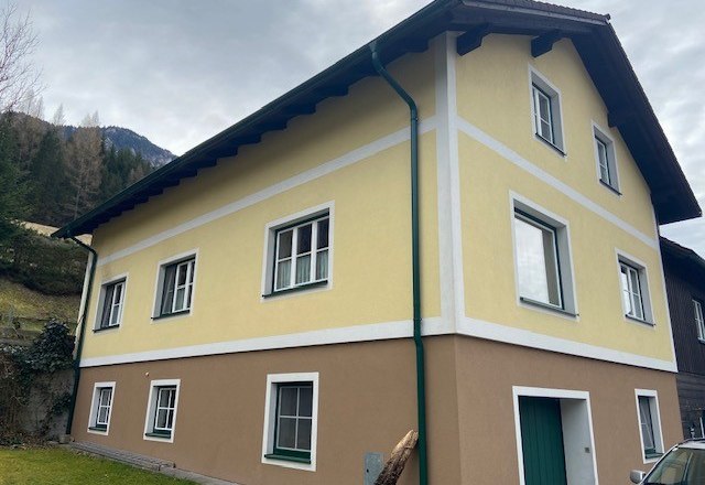 Zweist&ouml;ckiges gelb-braunes Haus mit wei&szlig;en Fensterrahmen und gr&uuml;nem Fallrohr.