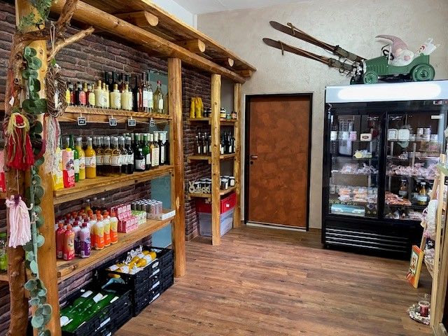 Innenansicht eines Hofladens mit Regalen voller Getränke und einem Kühlschrank mit Lebensmitteln.
