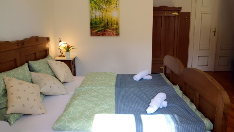 Gem&uuml;tliches Doppelzimmer mit Holzm&ouml;beln, gr&uuml;nem Bettzeug und einem Bild an der Wand.