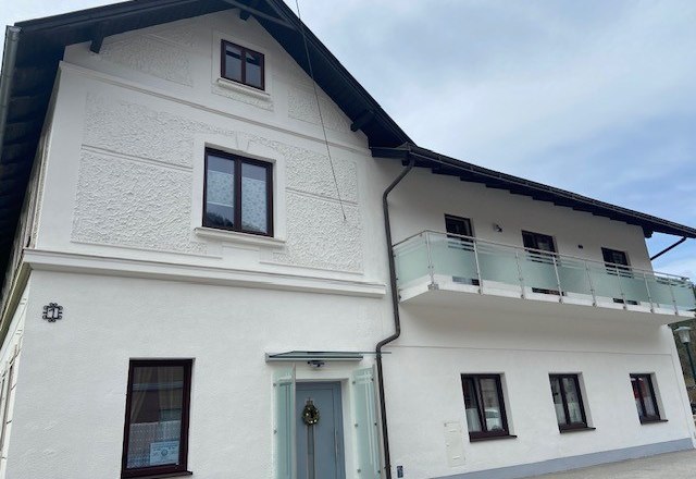 Zweist&ouml;ckiges wei&szlig;es Haus mit Balkon und mehreren Fenstern.